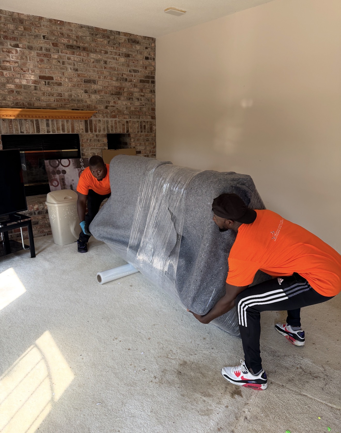 Two Burray movers lifting a blanket wrapped and shrink wrapped sofa
